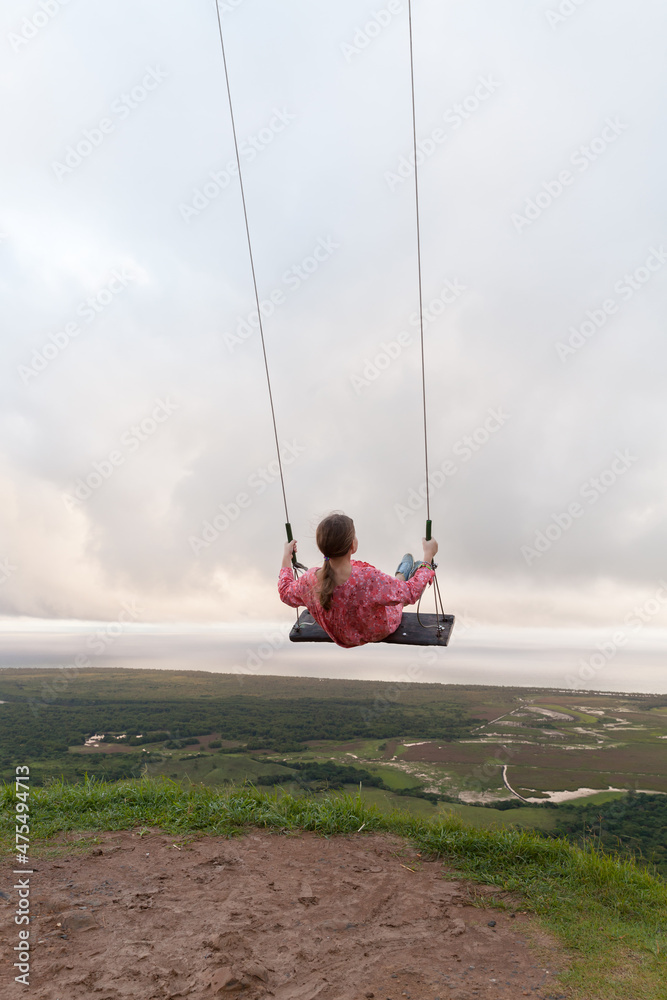 Little girl is on a swing under cloudy sky at the top of the mountain