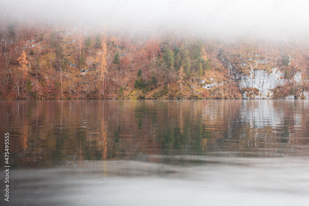 Fog on lake Kenigsee, Germany. Mist on lakeshore with forest reflection in water. Tranquil German landscape with haze. Autumn scenery in Europe, national Berchtesgaden park. Autumn nature. 