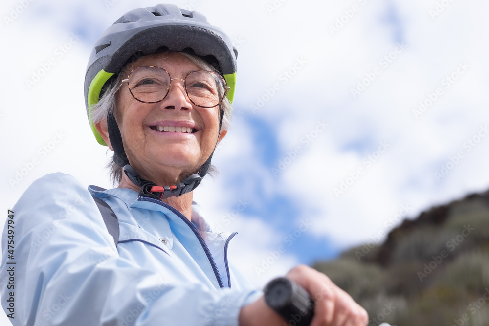 Portrait of smiling senior biker woman wearing sport helmet and eyeglasses in outdoors excursion Portrait of smiling senior biker woman wearing sport helmet and eyeglasses in outdoors excursion