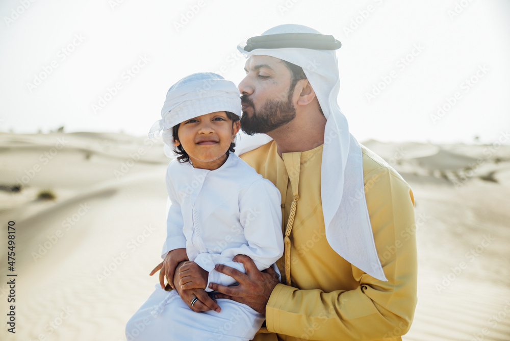 Father and son spending time in the desert on a safari day. Arabian family from the emirates wearing the traditional white dress. Concept about lifestyle and middle eastern cultures