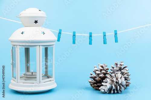 White lantern with candle inside and Christmas decoration on blue background. Copy space.