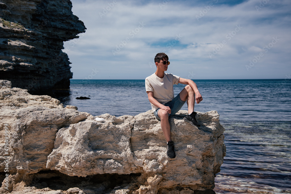 Young man next to the rock and the sea. Travel and vacation.