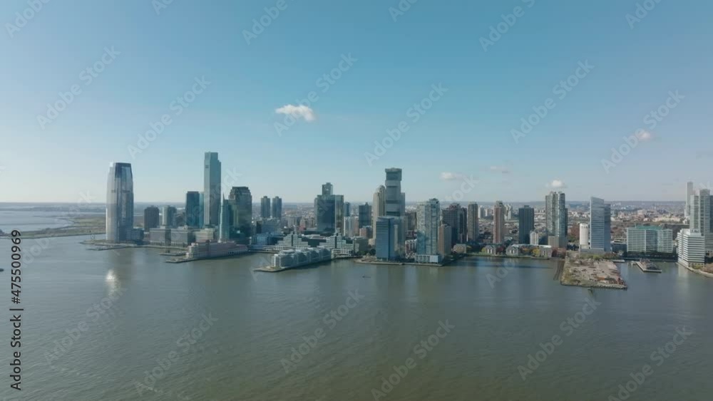 Forwards fly above water. Panoramic shot of downtown buildings on riverbank. Modern tall skyscrapers. Jersey City, USA Forwards fly above water. Panoramic shot of downtown buildings on riverbank. Modern tall skyscrapers. Jersey City, USA