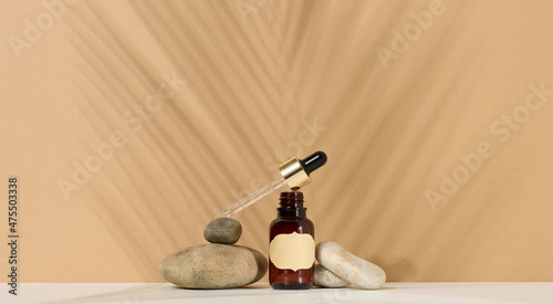 a brown glass bottle with a pipette and a brown label stands on a stone. Container for cosmetics, serum and oil. Palm leaf shadow