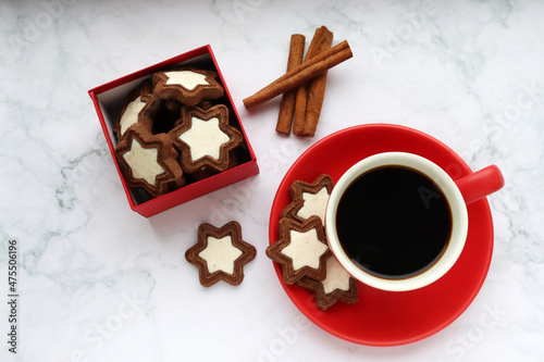 Cup of coffee with star shaped cookies, cinnamon sticks and christmas decorations on white marble table. Christmas background. Top view, copy space. Flat lay winter holidays composition