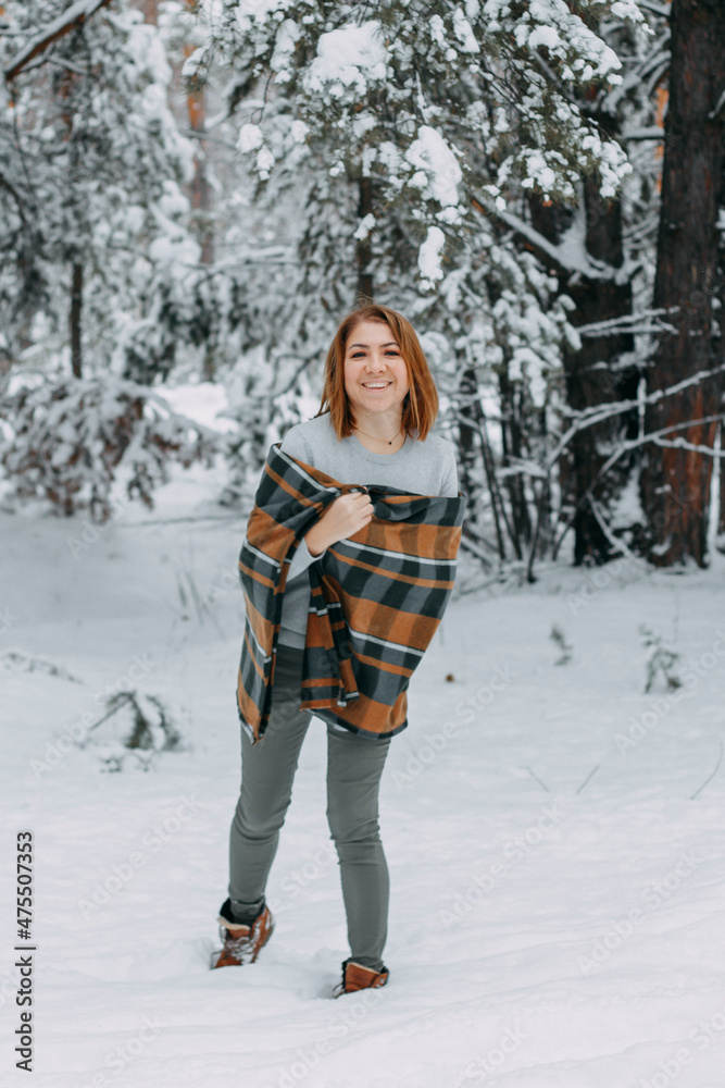 A happy young girl, wrapped in a plaid plaid and basking on a walk in the winter forest. A walk in the Christmas holidays, selective focus