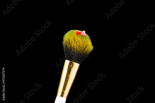 Two red hearts on a brush for powder and makeup, on a black background, close-up.