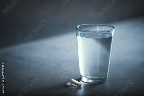 Glass of fresh water and medicine on a dark table. Daily routine of drinking and eating pills. 