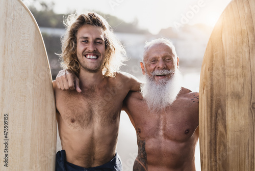 Happy fit surfers with different ages having fun surfing on tropical beach - Extreme sport lifestyle and friendship concept