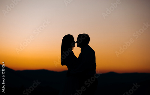 Groom and bride stand on the mountain against the background of sunset