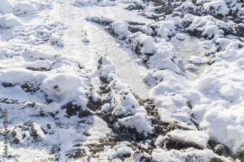 Frozen mud under a layer of fresh snow. Close-up of a bad suburban dirt road. Selective focus