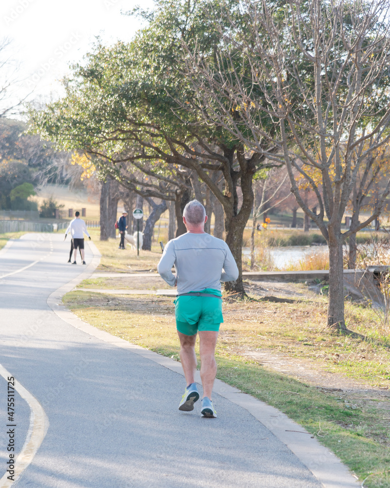 Fototapeta premium Rear view senior man in long sleeve shirt and short running on sidewalk near White Rock Lake park in fall season Dallas, Texas