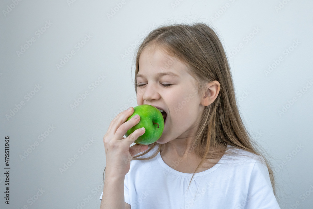 Cute little girl in white T-shirt eating green apple. Health care, fruits, healthy eating, dental care for kids. child bites an apple. Cute little girl in white T-shirt eating green apple. Health care, fruits, healthy eating, dental care for kids. child bites an apple.
