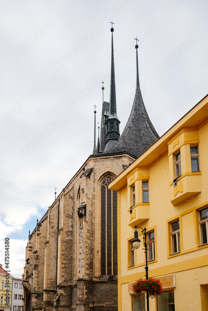 Louny, Czech Republic, 19 September 2021: Medieval catholic stone church of St. Nicholas with gothic high spire clock tower in autumn day, Narrow picturesque street in historic city center, arches
