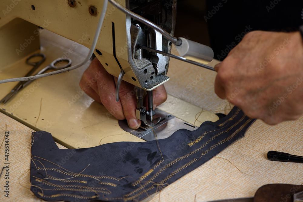 Mechanic repairing industrial sewing machine in factory. Hands of repairman fixing problems and testing professional overlock in shoemaker workshop. Closeup