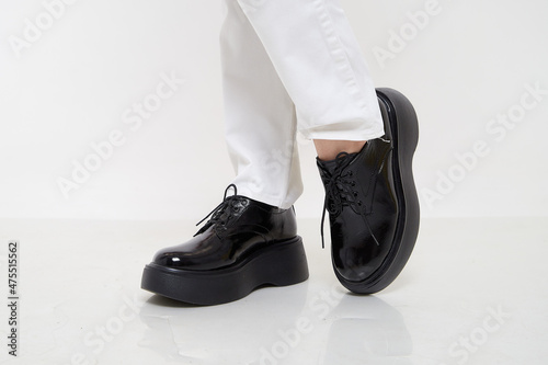 Black female or male patent leather shoes on legs of woman. Shooting for a catalog or an online store. A pair of shoes