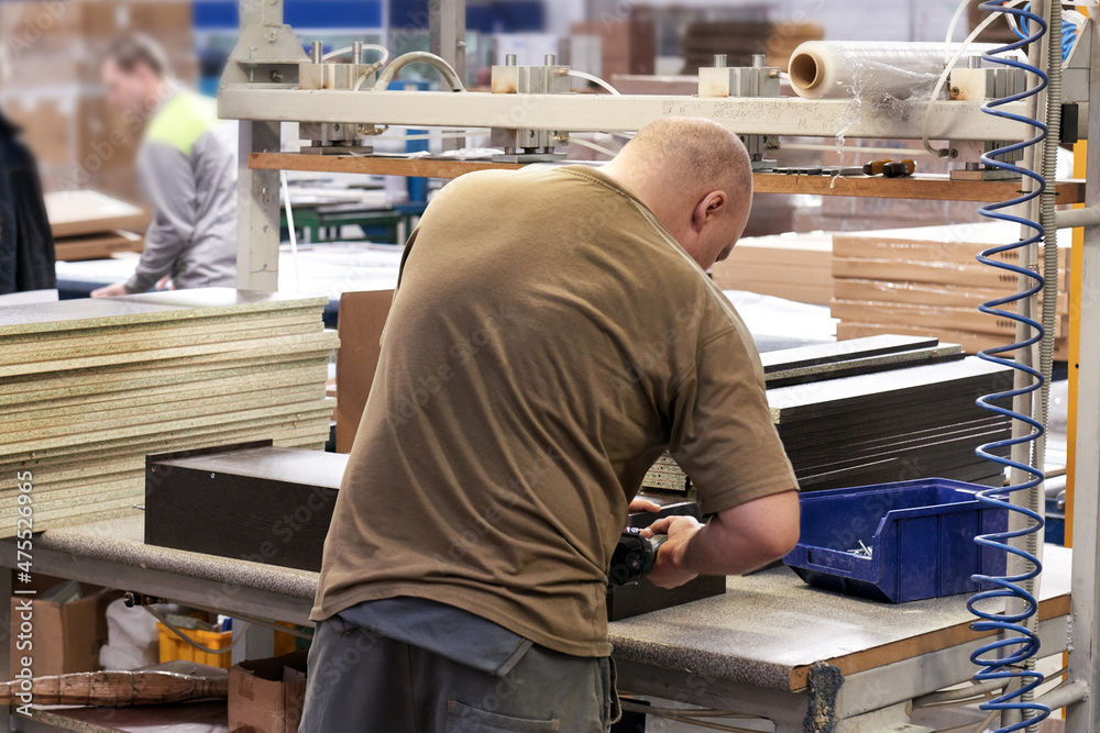 A worker assembles furniture at a factory. Industrial production of furniture.