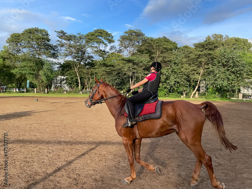 A child wearing Horse riding protective gear riding a brown horse in a ranch