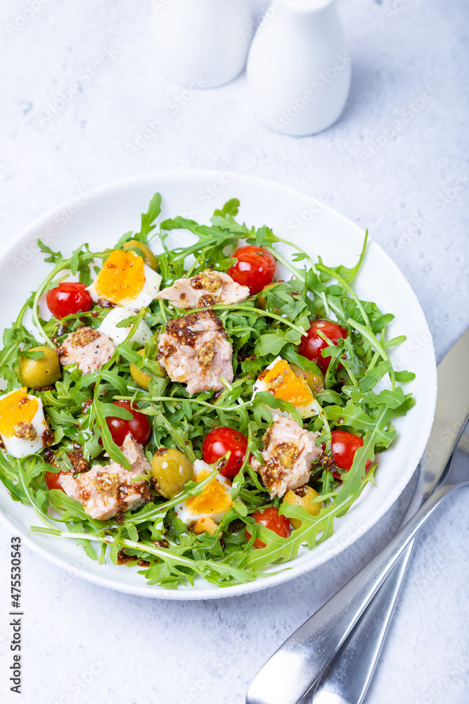 Salad with tuna, arugula, tomatoes, olives and eggs in a white plate. A traditional dish. Close-up. Salad with tuna, arugula, tomatoes, olives and eggs in a white plate. A traditional dish. Close-up.