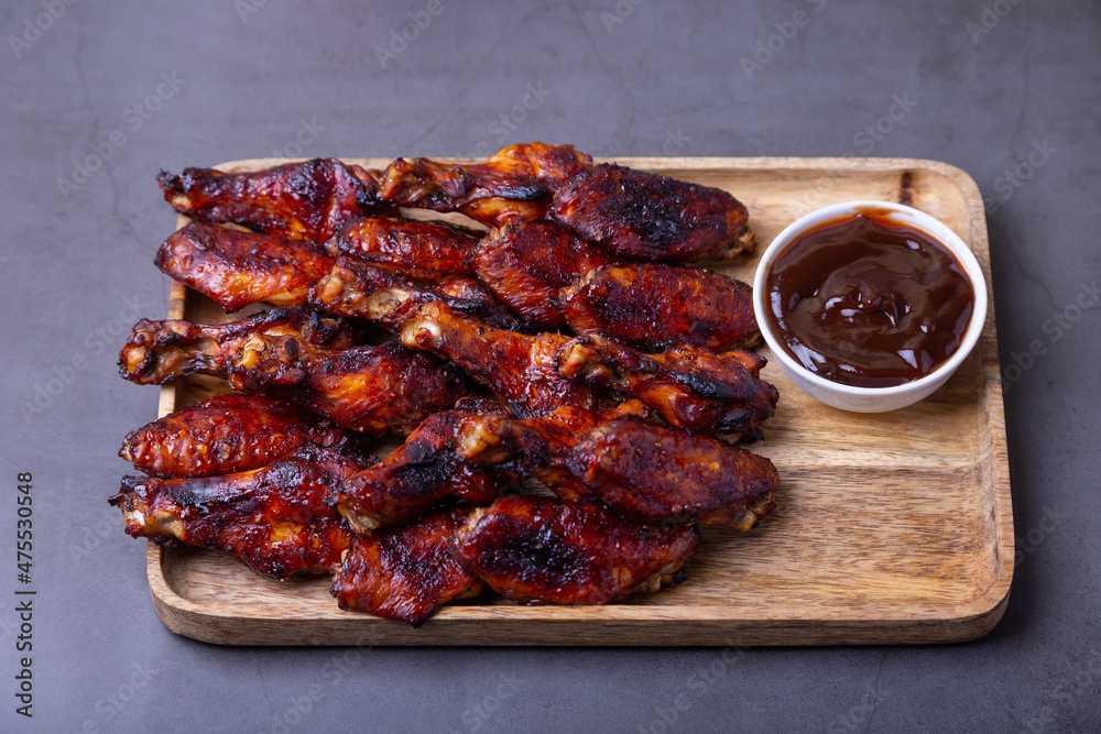Fried chicken wings on a wooden board with barbecue sauce. Black background, close-up.