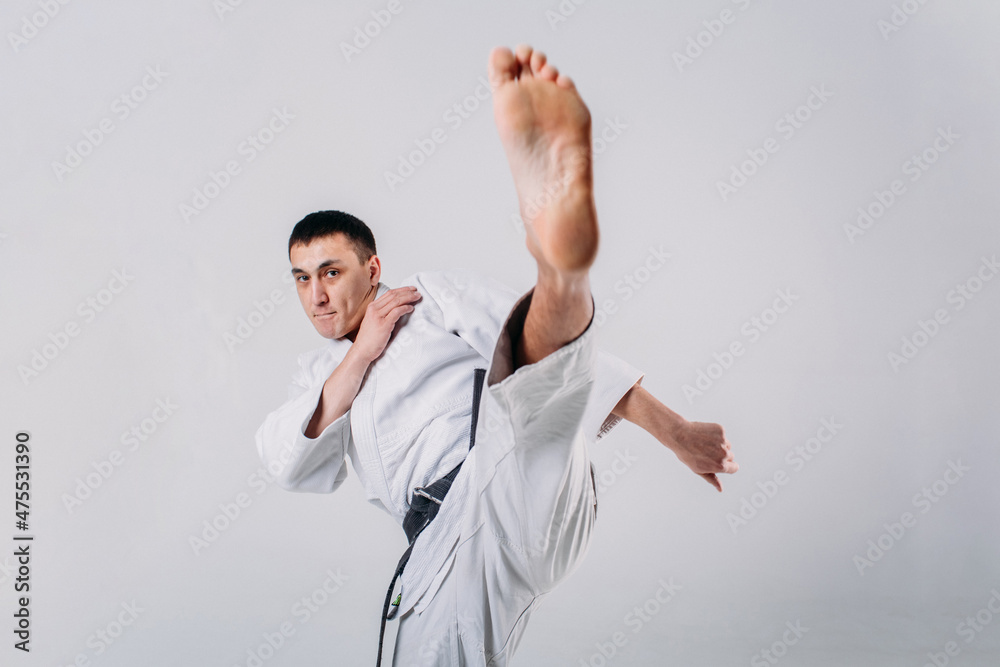 a young man, in a white kimano, shows the elements of karate in the studio on a white background a young man, in a white kimano, shows the elements of karate in the studio on a white background