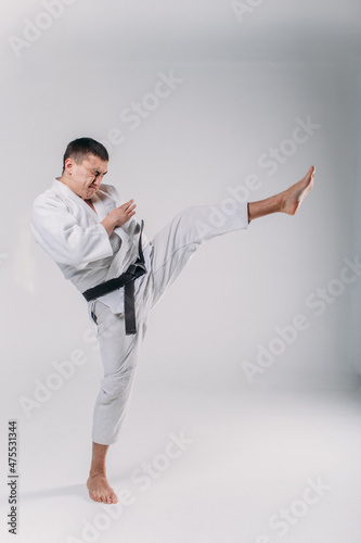 a young man, in a white kimano, shows the elements of karate in the studio on a white background