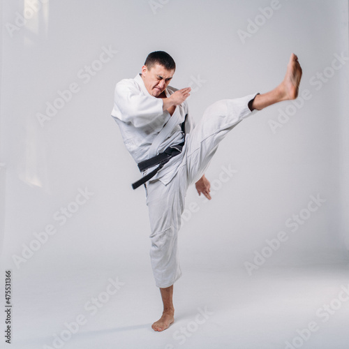a young man, in a white kimano, shows the elements of karate in the studio on a white background