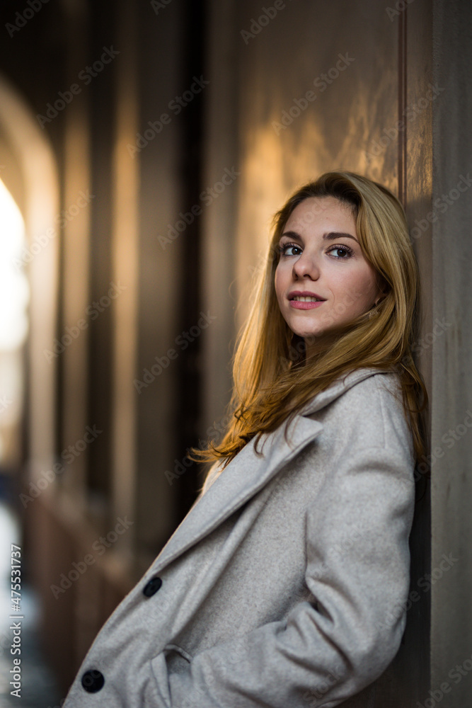 smiling blonde teenage girl in coat leaning on the wall in the street