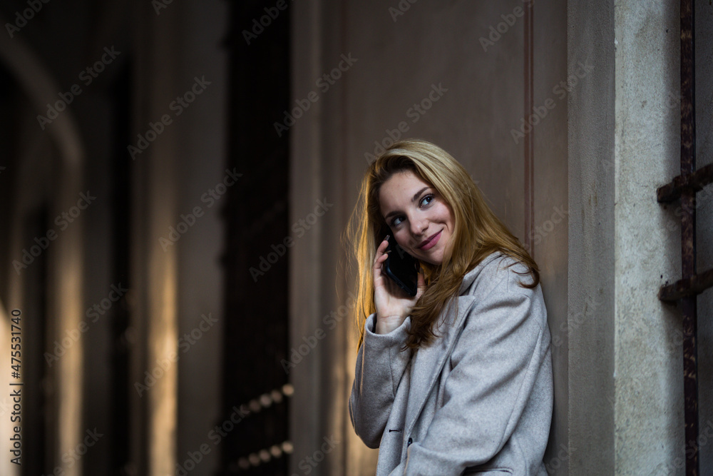 smiling blonde teenage girl talking with her smartphone in the street