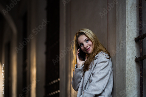 smiling blonde teenage girl talking with her smartphone in the street