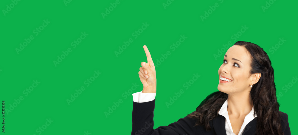 Happy smiling looking up woman in black confident suit, showing pointing at copy space. Business concept. Green colour background. Attractive brunette businesswoman. Happy smiling looking up woman in black confident suit, showing pointing at copy space. Business concept. Green colour background. Attractive brunette businesswoman.