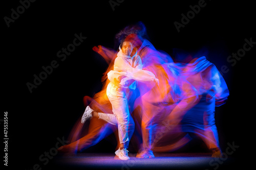 Stylish young girl in white costume dancing hip-hop dance isolated on dark background at dance hall in neon mixed light.