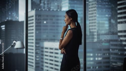 Successful Businesswoman in Stylish Dress Working on Laptop, Looking out of the Window at Big City. Confident Female CEO Analyze Financial Projects. Manager at Work Planning Marketing Campaign.