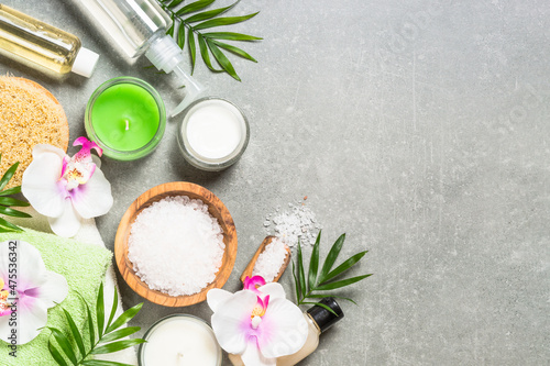 Spa product composition with palm leaves, towel, bath salt and cosmetic at gray stone table. Healthcare concept. Flat lay image with copy space.