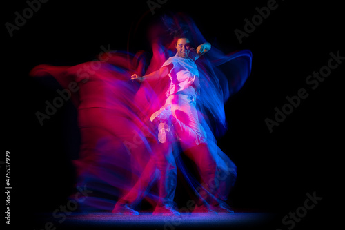 Emotional young girl in white costume dancing hip-hop dance isolated on dark background at dance hall in neon mixed light.