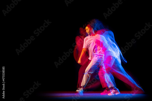 Sportive young girl in white costume dancing hip-hop dance isolated on dark background at dance hall in neon mixed light.