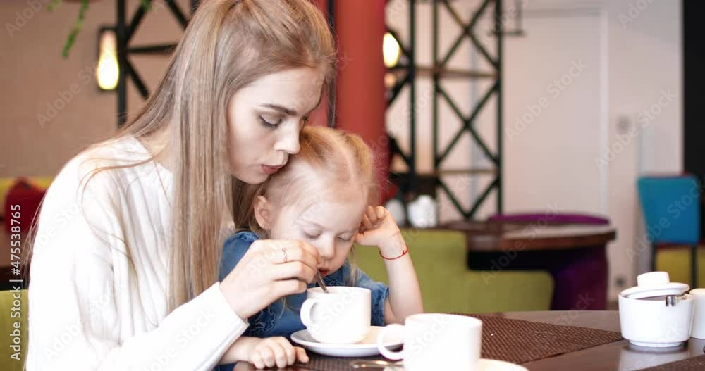 Mother and daughter are drinking tea in a cafe. Young family. Mother and daughter are drinking tea in a cafe. Young family.