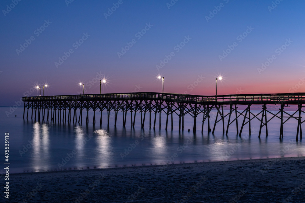 Fishing pier silhouette sunset blue hour orange and blue-sky lights shimming on the blurred waves Horizontal Photo, Photograph Holden Beach NC 