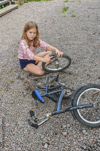 the child girl has damaged a bicycle wheel and is making repairs photo without processing