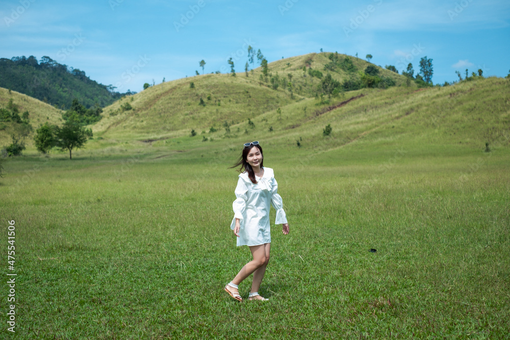 Beautiful Girl stand and acting in front of bald mountain or Phu Khao Ya with green grass field and blue sky. One of natural travel attraction in Ranong province, Thailand Beautiful Girl stand and acting in front of bald mountain or Phu Khao Ya with green grass field and blue sky. One of natural travel attraction in Ranong province, Thailand