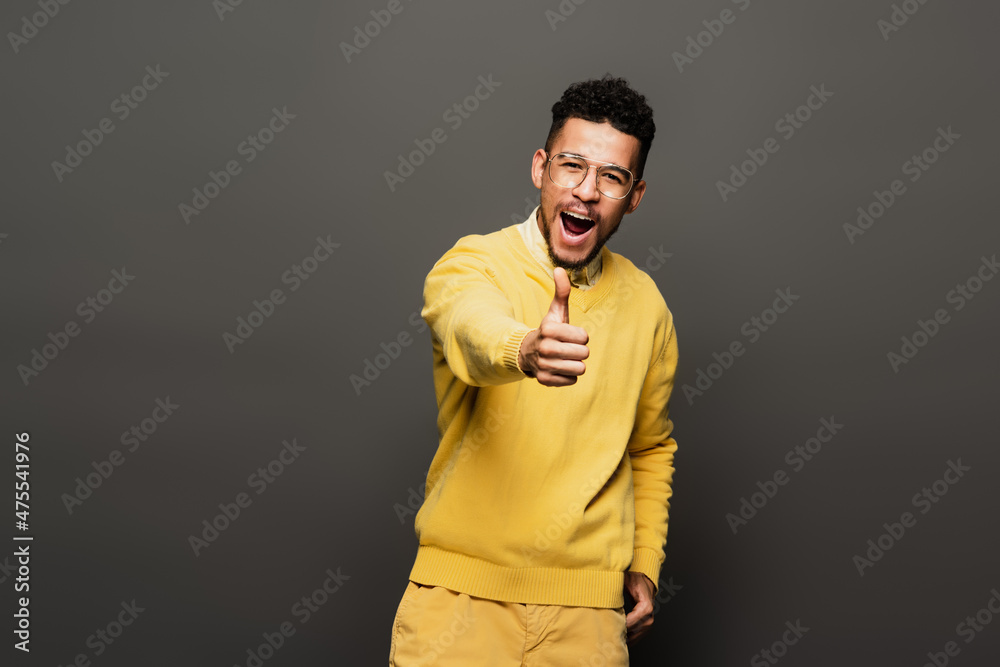amazed african american man in glasses showing thumb up on dark grey. amazed african american man in glasses showing thumb up on dark grey.