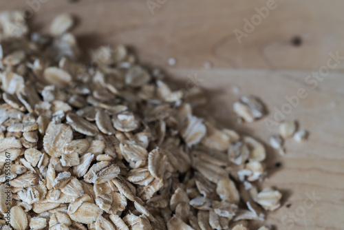 closeup pile of rolled oats on a light wooden surface with a muted natural color palette - ingredient for cooking or baking