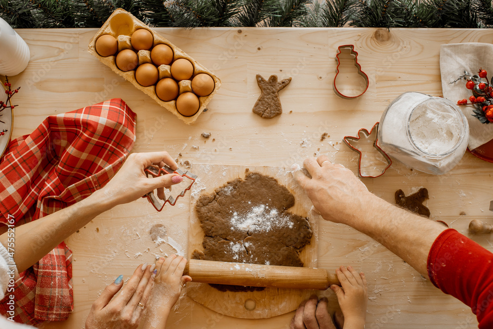 Fototapeta premium Close up of young family's hands prepare christmas cookies on a wooden table with a lot of cooking ingredients.