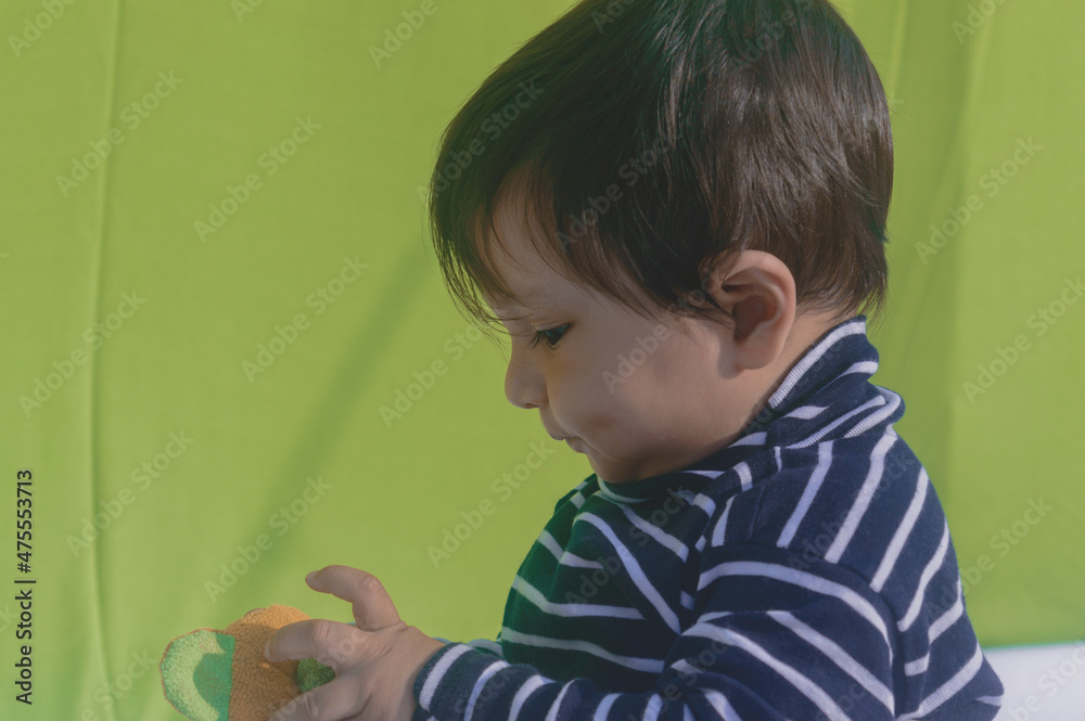 Happy Beautiful Cute Baby holding a toy and Looking down. Head shot portrait. Side View. Close up. Indian ethnicity. Isolated on light green background. Happy Beautiful Cute Baby holding a toy and Looking down. Head shot portrait. Side View. Close up. Indian ethnicity. Isolated on light green background.