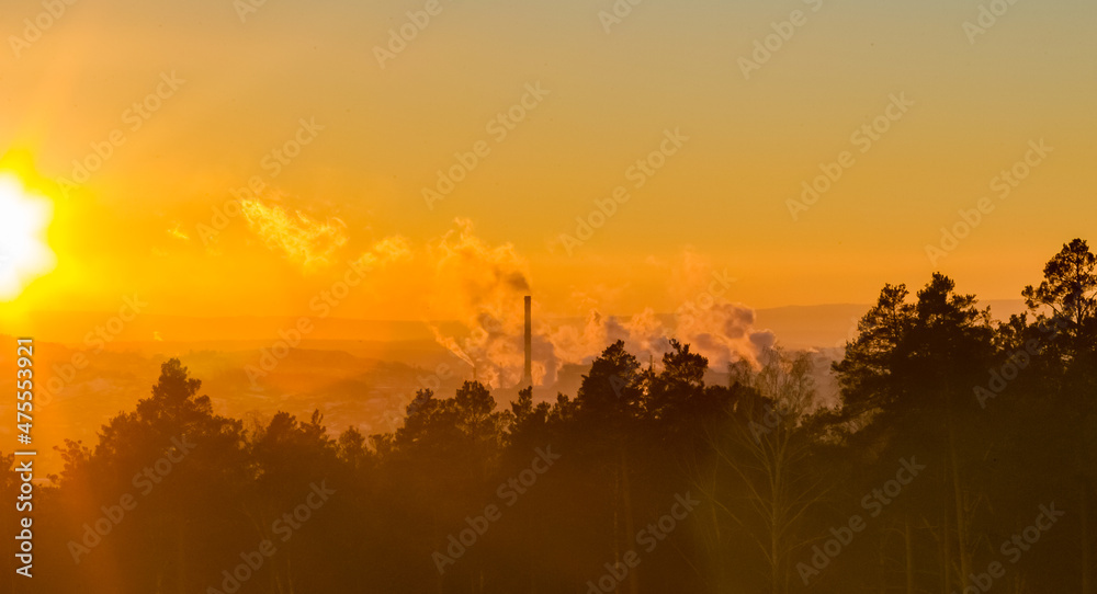 Trees and Chimneys with smoke on the background of mountains and the sunset sky in winter
