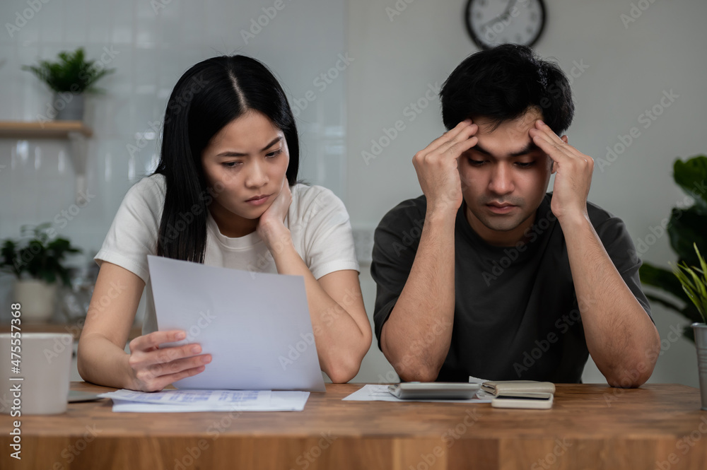 Portrait photo of young Asian couple feeling sad or worry about their financial situation because too many daily expense. Young couple consulting and discussing about family expenditure. Portrait photo of young Asian couple feeling sad or worry about their financial situation because too many daily expense. Young couple consulting and discussing about family expenditure.