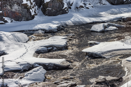 Fast river, rocks, ice, snow, dry grass in spring