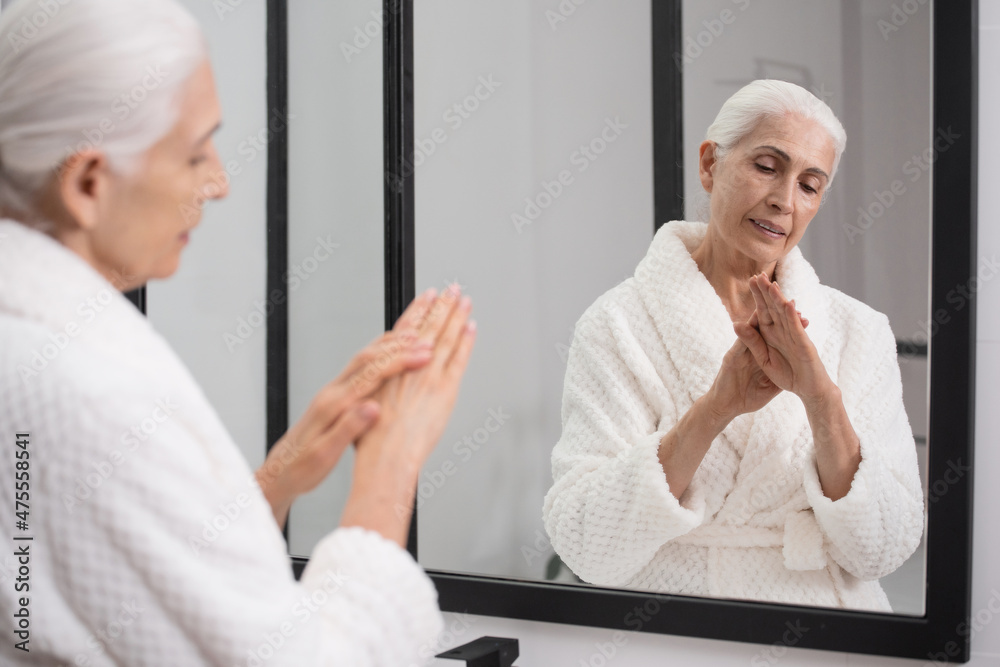 Obraz premium Aged woman looking at hands in front of mirror
