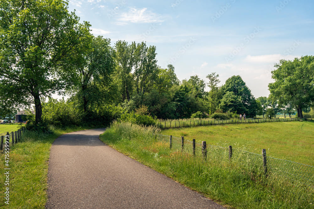 Dutch landscape with a curved country road. Completely in the background and unrecognizable, two people cycle in the direction of the photographer. The photo was taken on a sunny day in springtime.