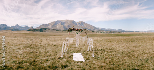 Wedding arch decorated with red flowers and macrame stands in a field against a background of mountains photo